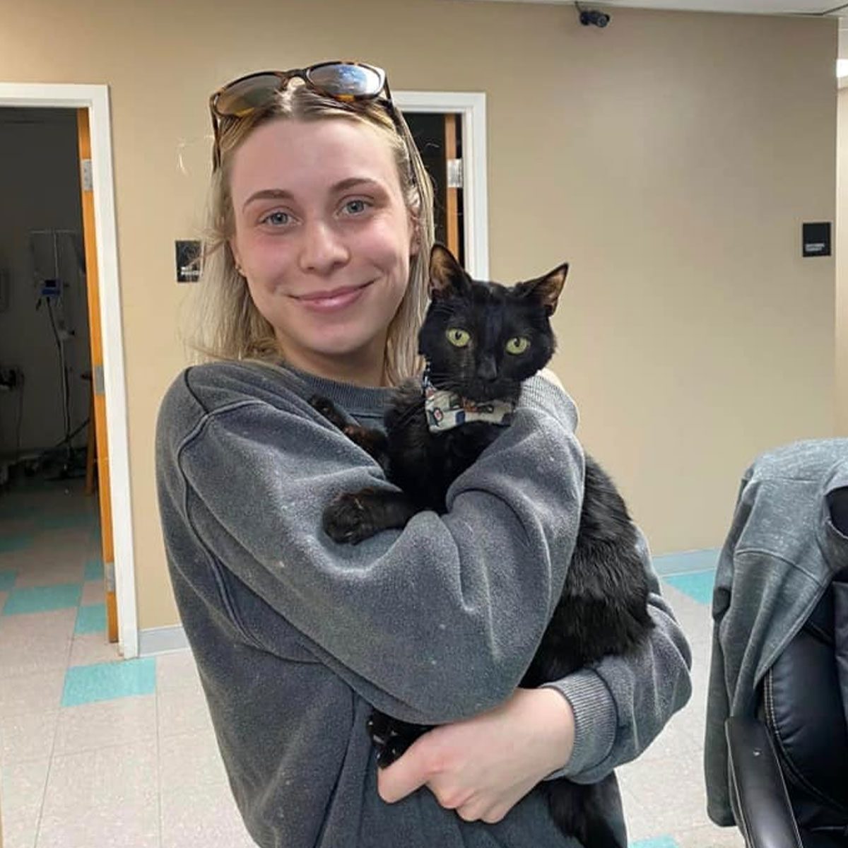 female staff member smiling and hugging black cat indoors